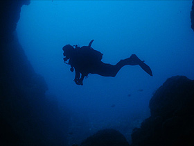 Diver swimming in front of a cave in the twilight hours